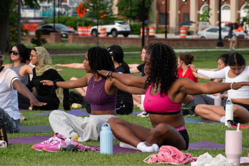Participants sitting down on yoga mats with outstretched arms during an outdoor pilates class