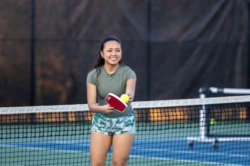 Pickleball participant holding a pickleball paddle and ball on the court