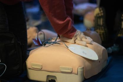 preson with a red long sleep shirt practicing CPR on a mannequin. The mannequin has AED pads on 