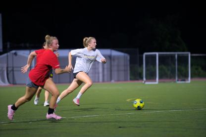 two soccer players, one with a red shirt and one with a white shirt running towards a yellow ball