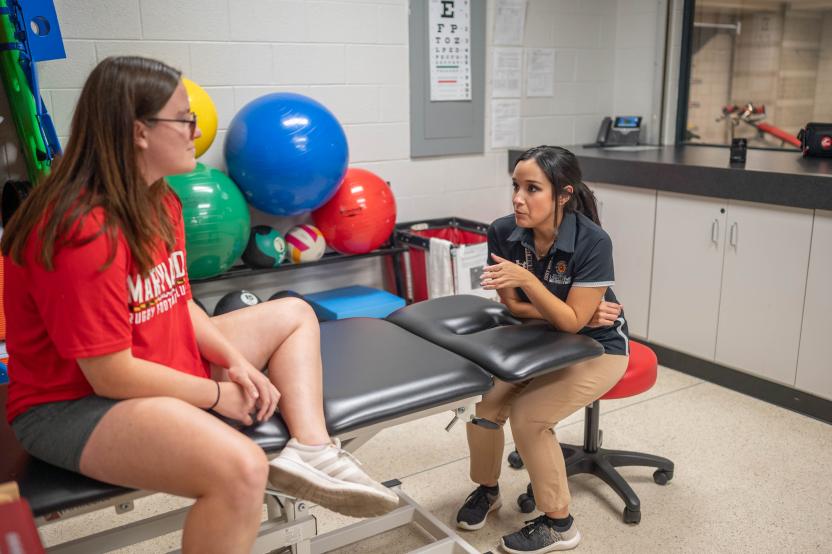 An athletic trainer sits with a student, reviewing their injury history in the clinic.
