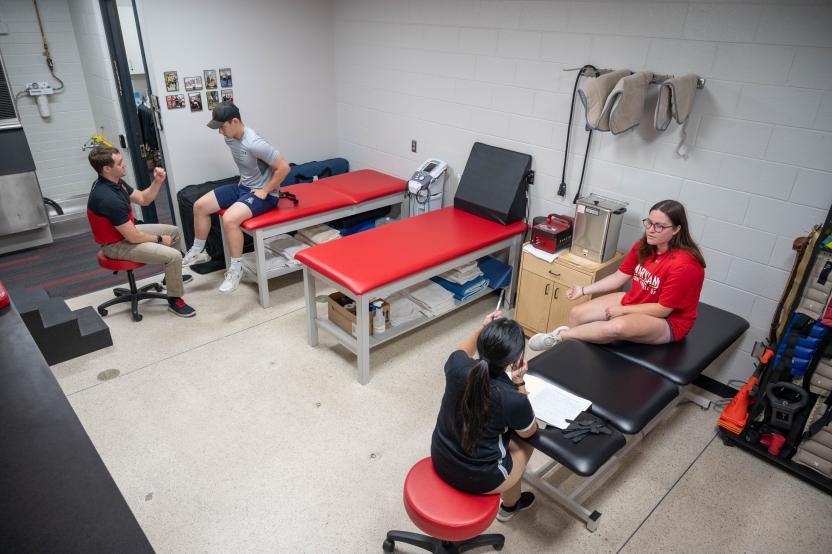 Two athletic trainers each evaluate one student as they sit on the treatment tables in the athletic training clinic.
