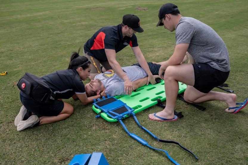 Two athletic trainers and one bystander practice safe cervical spine stabilization and spine boarding of a student.
